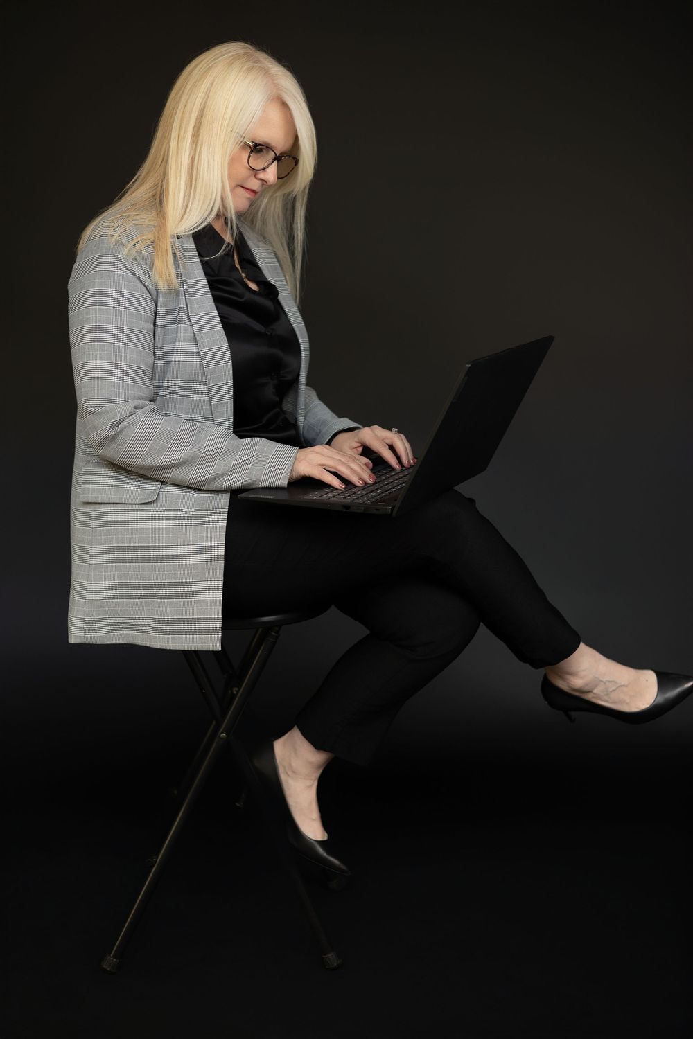 Professional woman in business attire working on laptop against dark background.