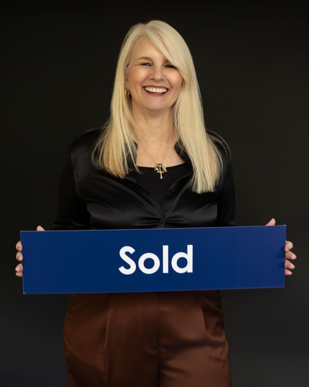 Business professional holding blue 'Sold' sign against dark background.