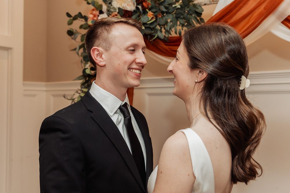 A joyful moment between a couple in formal wedding attire as they share a laugh beneath festive decorations.