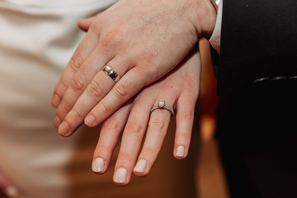 Two hands wearing matching wedding rings rest together against light and dark fabric backgrounds.