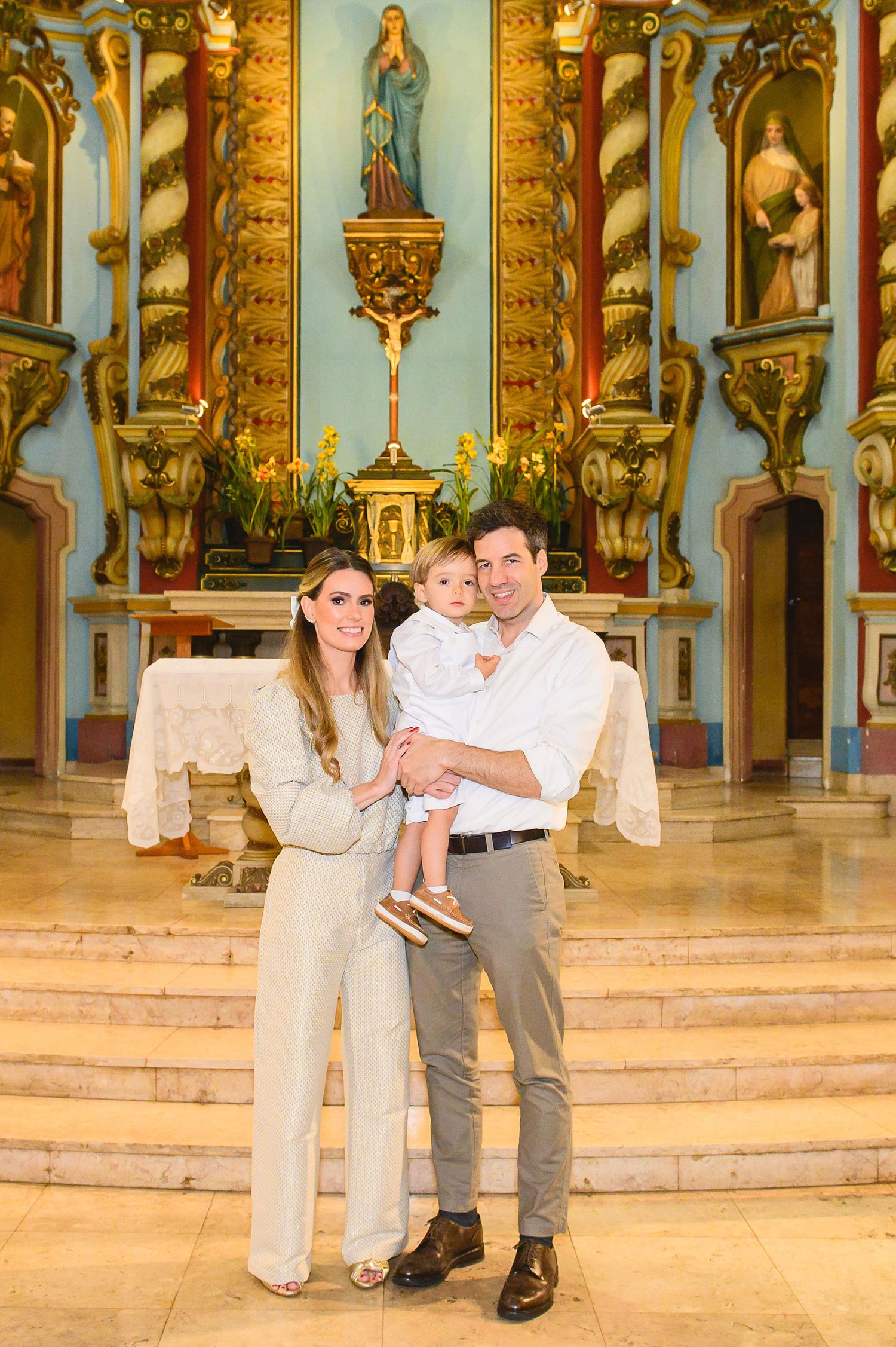 A family stands together at the altar of an ornate Catholic church with gilded decorations and religious statues.