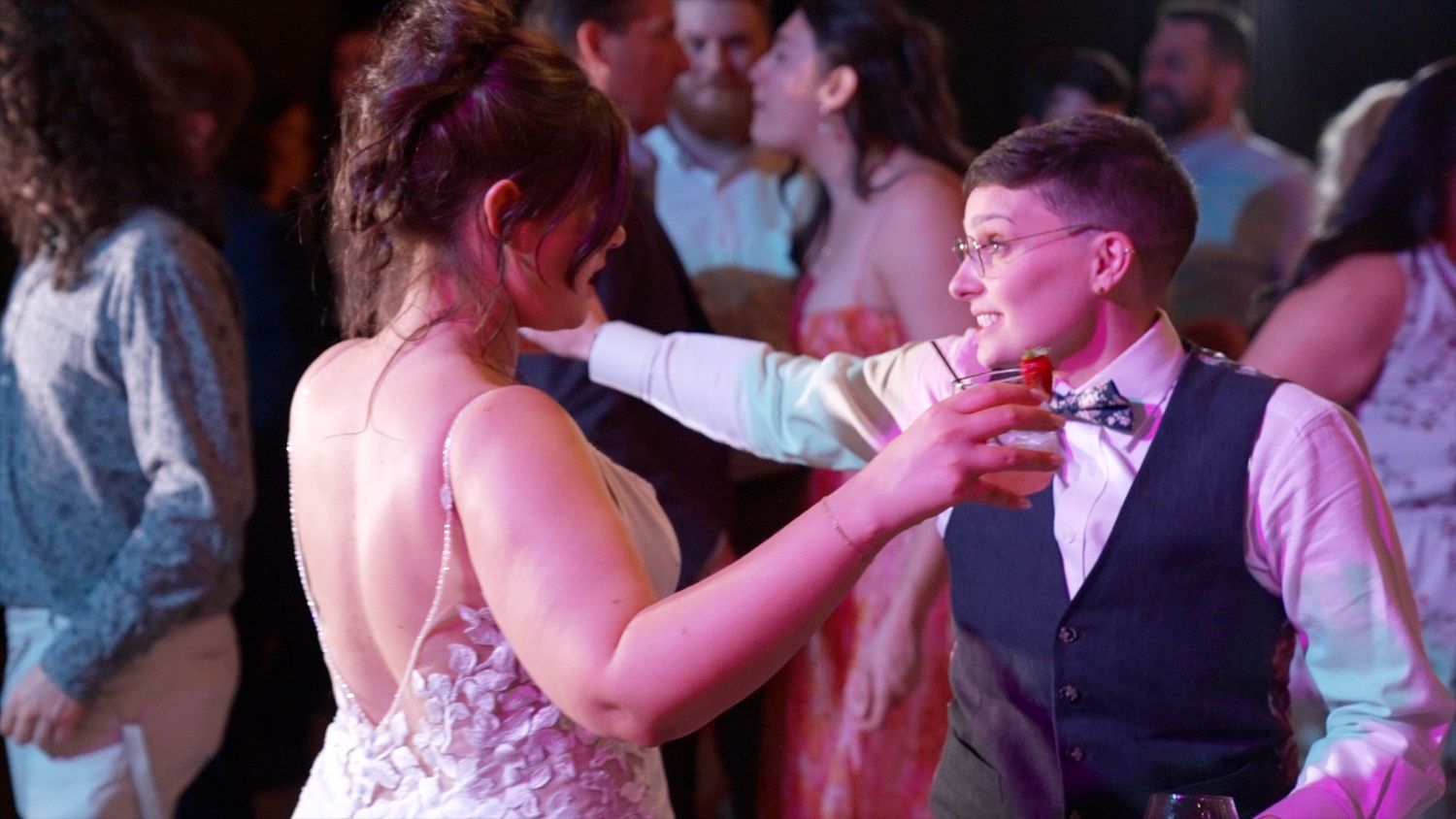 A couple shares an intimate dance moment at a wedding reception under pink and blue lighting.