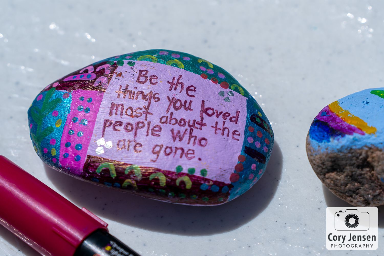 Inspirational quote painted on a colorful rock with a pen beside it on a light gray surface.