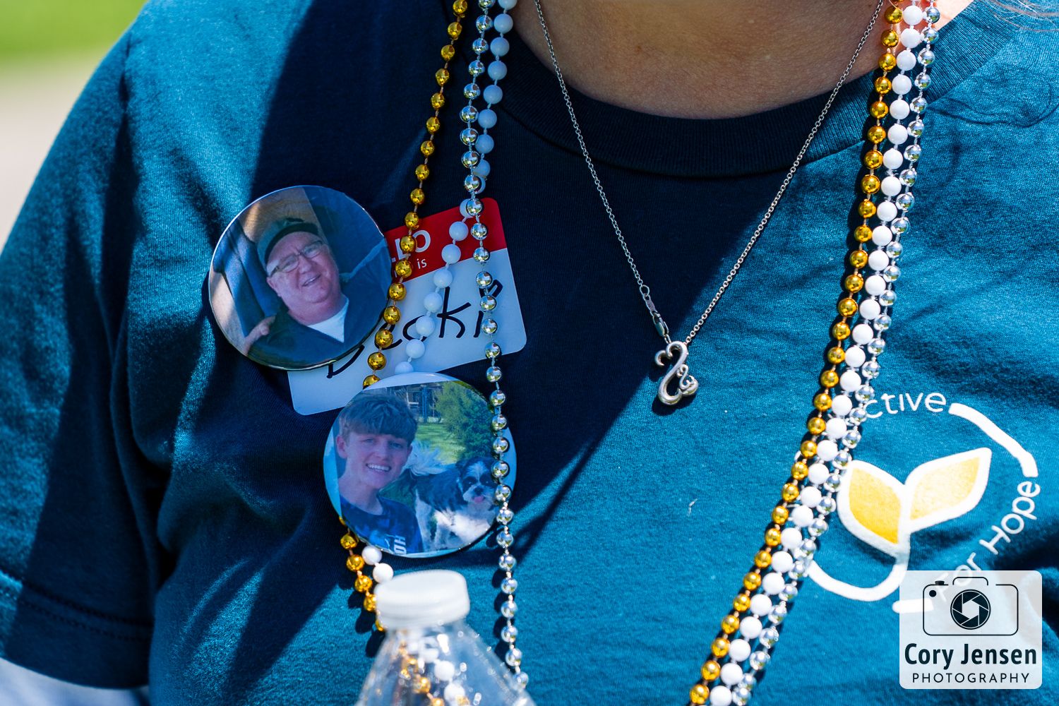 Close-up of pins and beads on a teal t-shirt with colorful decorative necklaces.