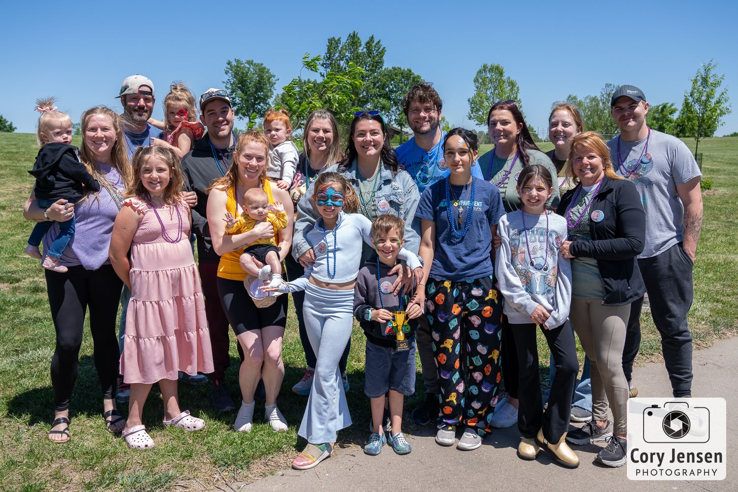 A large group of people gather outdoors on a grassy hill for a sunny day photo together.