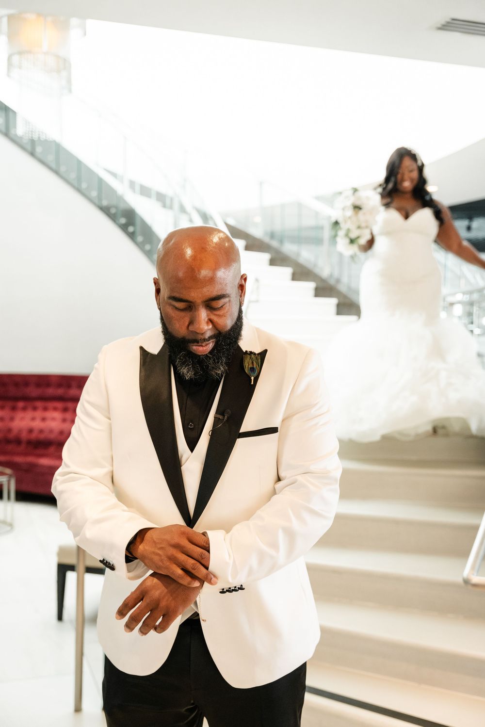 Emotional wedding day first look with groom in white tuxedo jacket and bride descending elegant staircase.