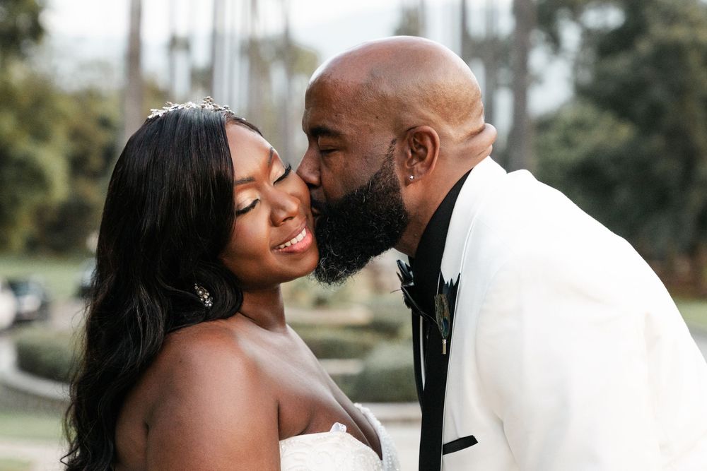 Couple shares an intimate wedding moment outdoors, with bride in white strapless gown and groom in black tuxedo.