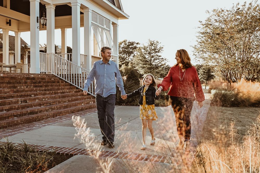 A family walks together on stone steps near a white columned porch during golden hour with tall grasses in the foreground.