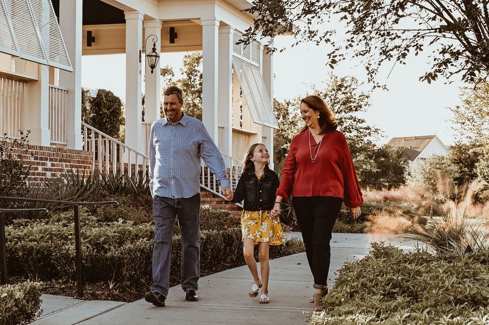 People walking together on a sidewalk path beside a classic white porch on an autumn afternoon.