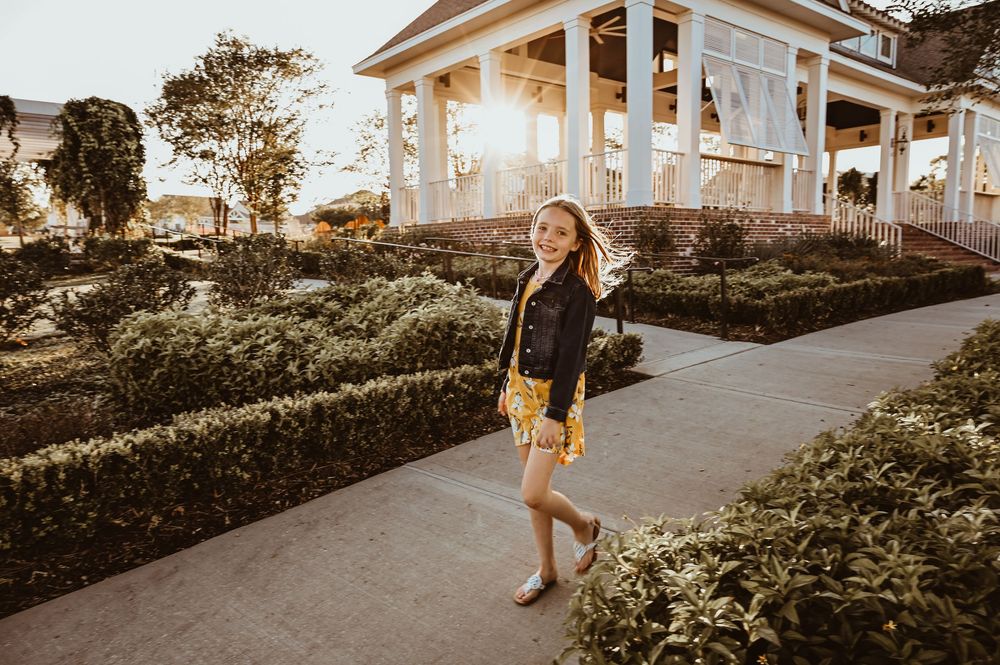 Person walking on sidewalk path beside manicured garden and white colonial style building at golden hour.