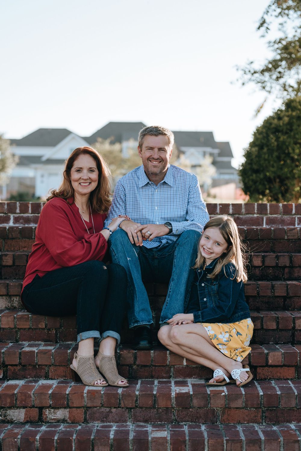 A family sitting together on red brick steps outside a residential home on a sunny day.