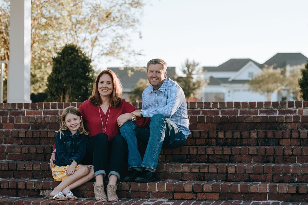 A family sits together on red brick steps outside during golden hour in a suburban neighborhood.