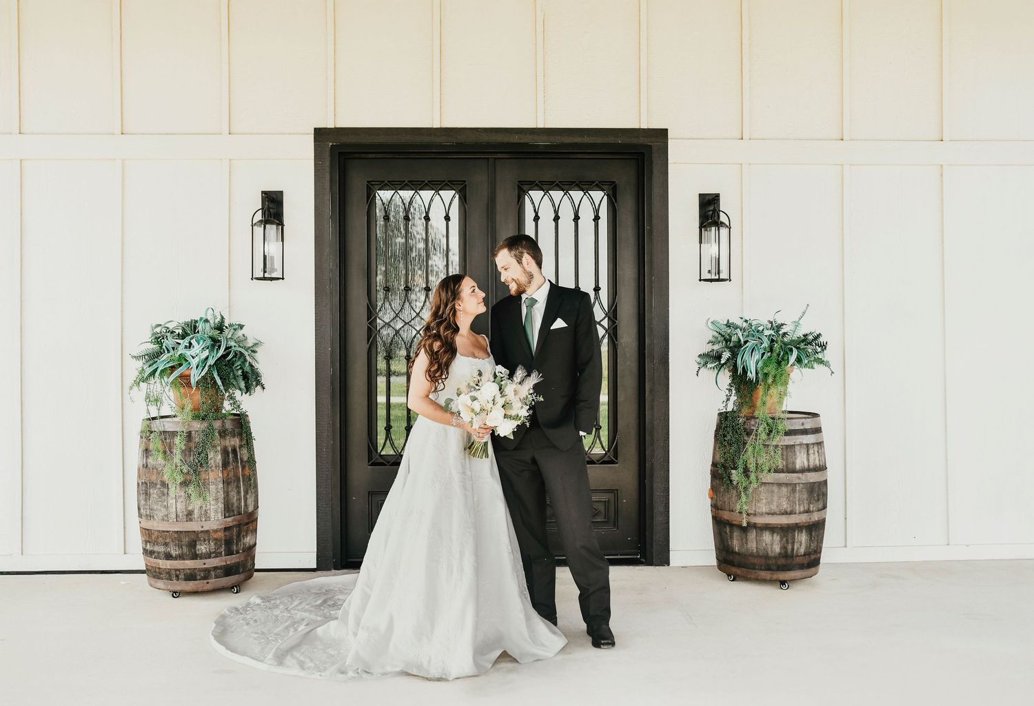 Full-length bridal portrait with groom and rustic Texas barn