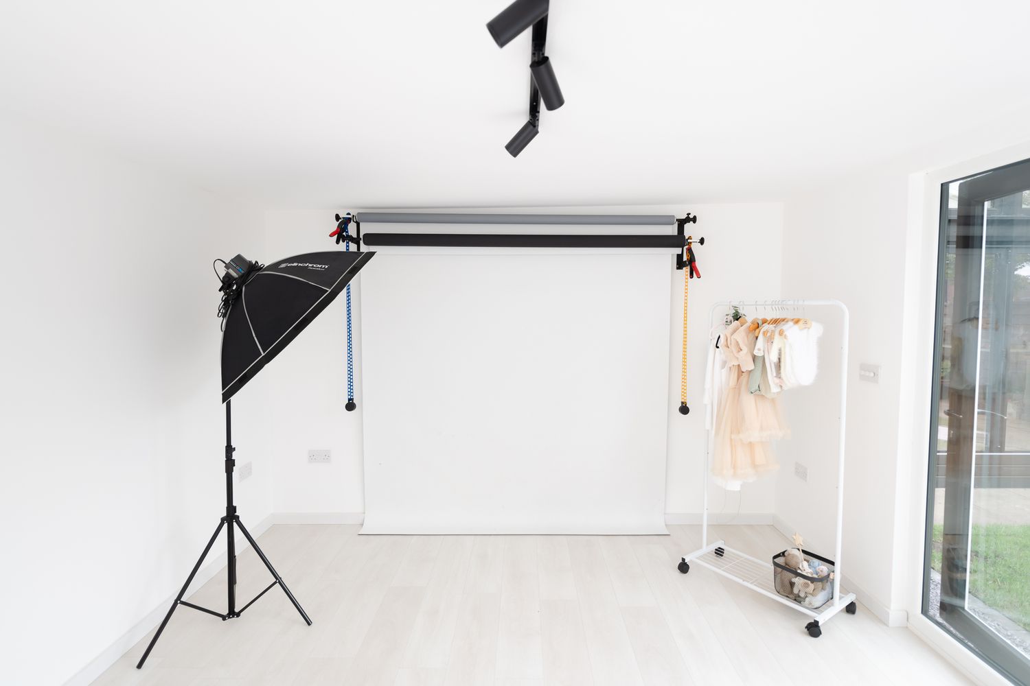 Minimalist white photography studio with backdrop stand, lighting equipment and natural window light.