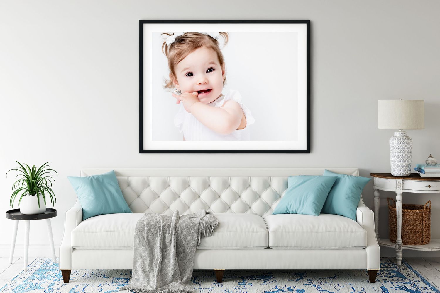 A framed photo displayed above a white tufted couch with turquoise pillows and gray throw in a modern living room.