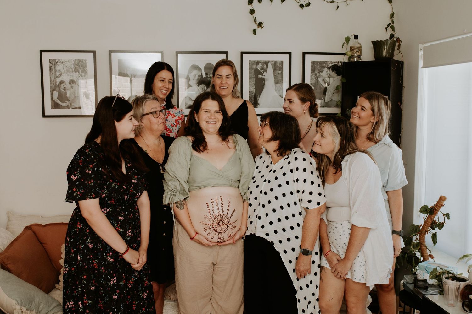 A group of women gather together in a warm indoor setting, with one wearing a sage green outfit in the center.