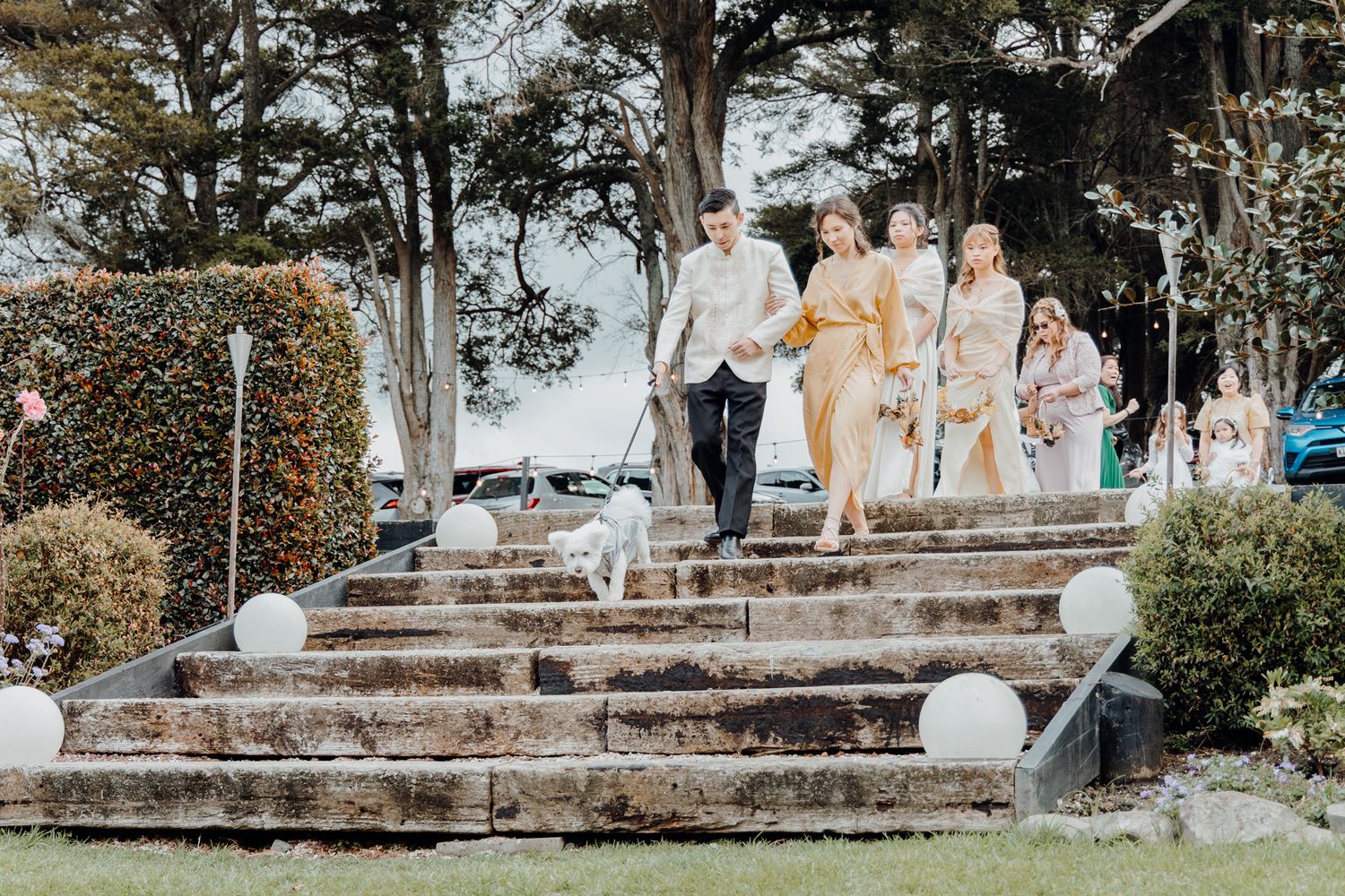 Wedding party members descend stone garden steps decorated with white balloons and floral arrangements.