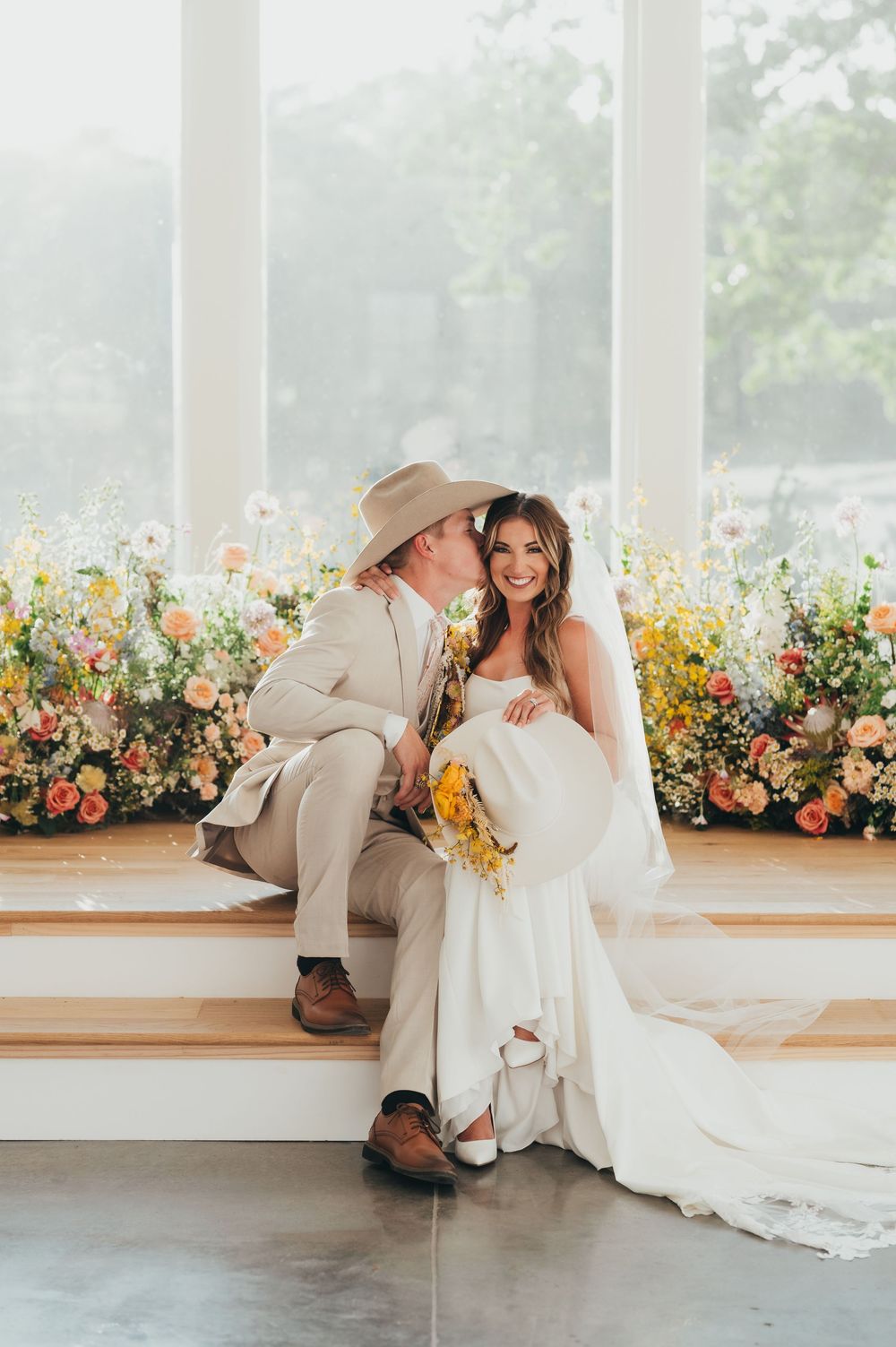 Newlyweds share an intimate moment on wooden steps surrounded by colorful floral arrangements.