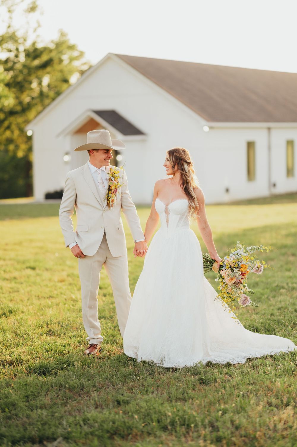 A rustic country wedding with the couple walking near a white chapel during golden hour sunset.