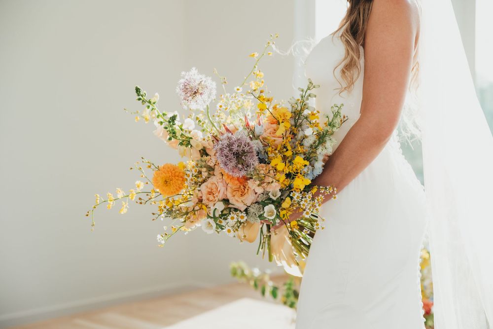 A delicate bridal bouquet featuring yellow, pink, and purple wildflowers arranged in a natural, rustic style.