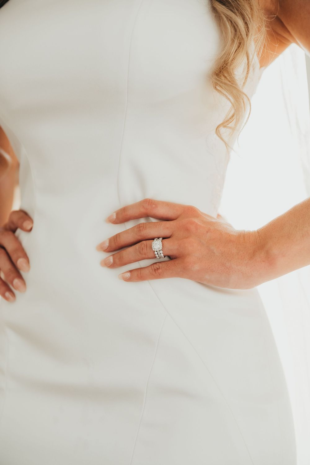 Close-up detail shot of a sparkling diamond wedding ring on a bride's hand against a white dress.
