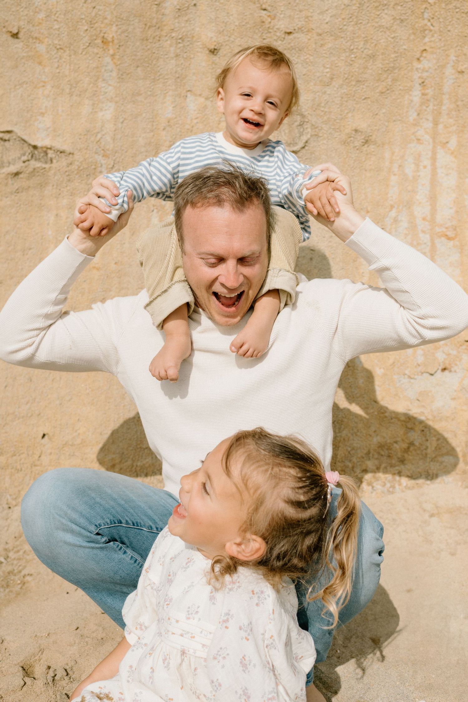 Joyful family moment with playful shoulder ride and laughter against textured beige wall.