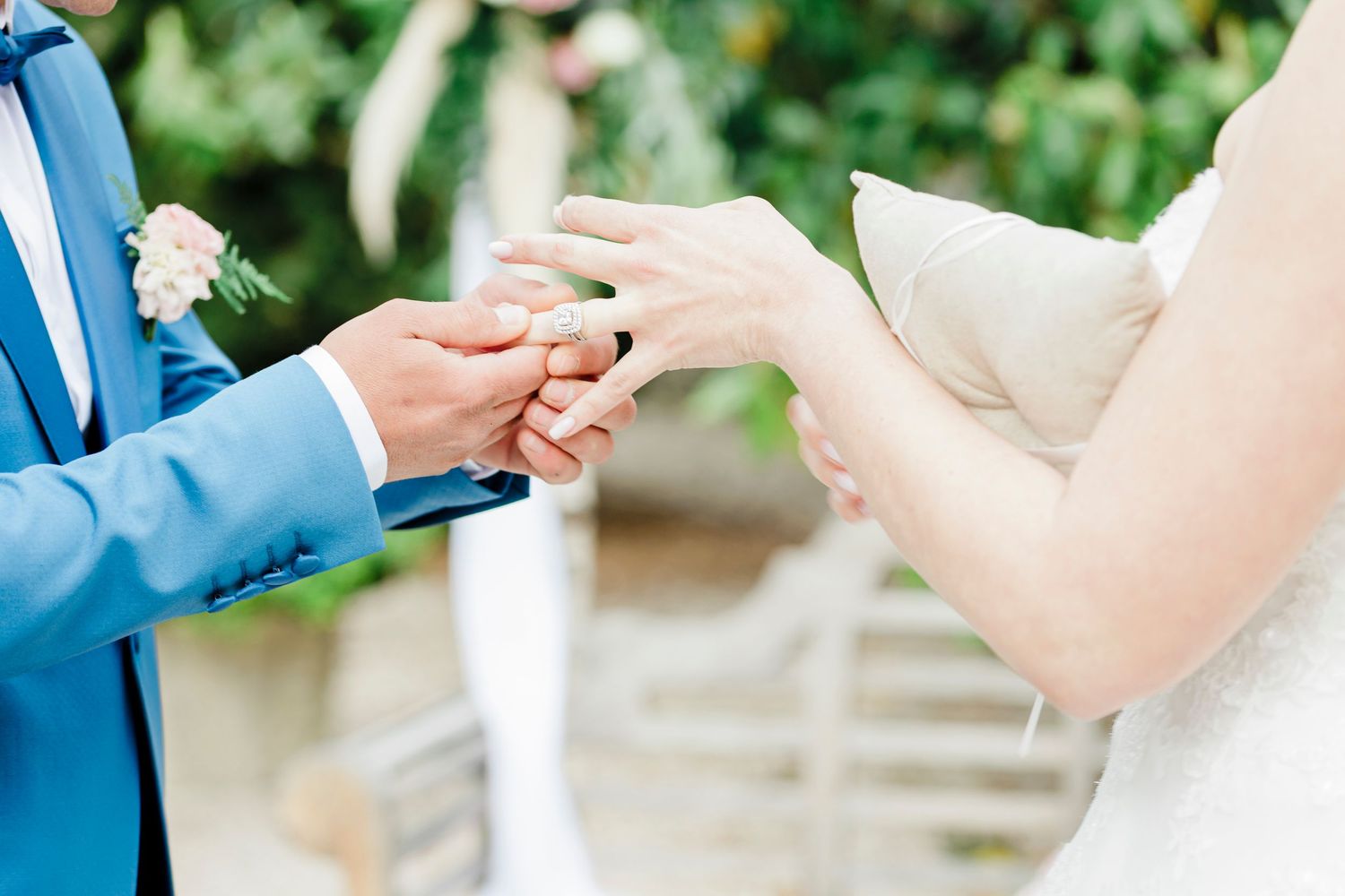 Wedding ring exchange between couple wearing light blue suit and white dress.