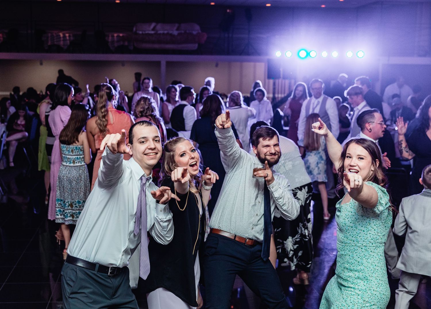 Energetic crowd dancing and having fun at a lively nighttime party with purple lighting and people in formal attire.