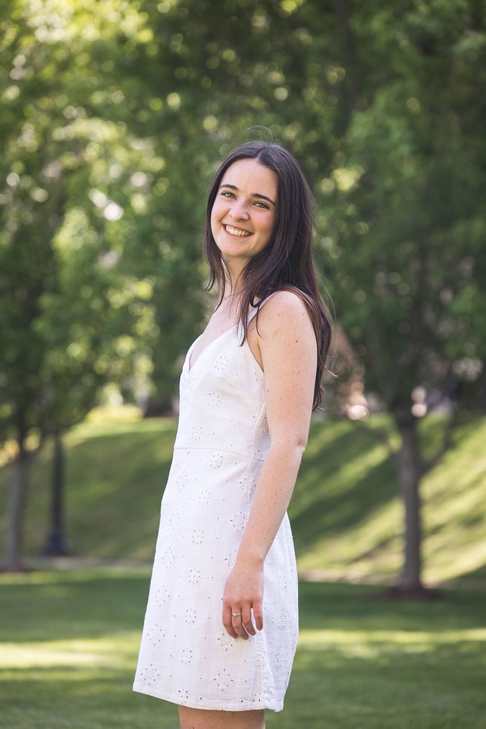 Person in a white eyelet lace summer dress smiles while standing in a sunny green park.