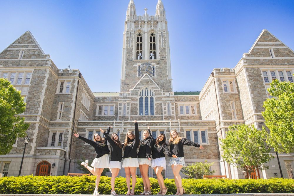 Group of students jumping joyfully in front of a Gothic university building with stone towers on a sunny day.
