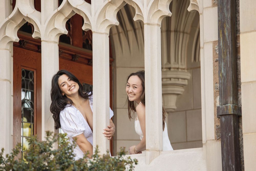 Two friends laughing and peeking through ornate white stone archways with decorative architecture.