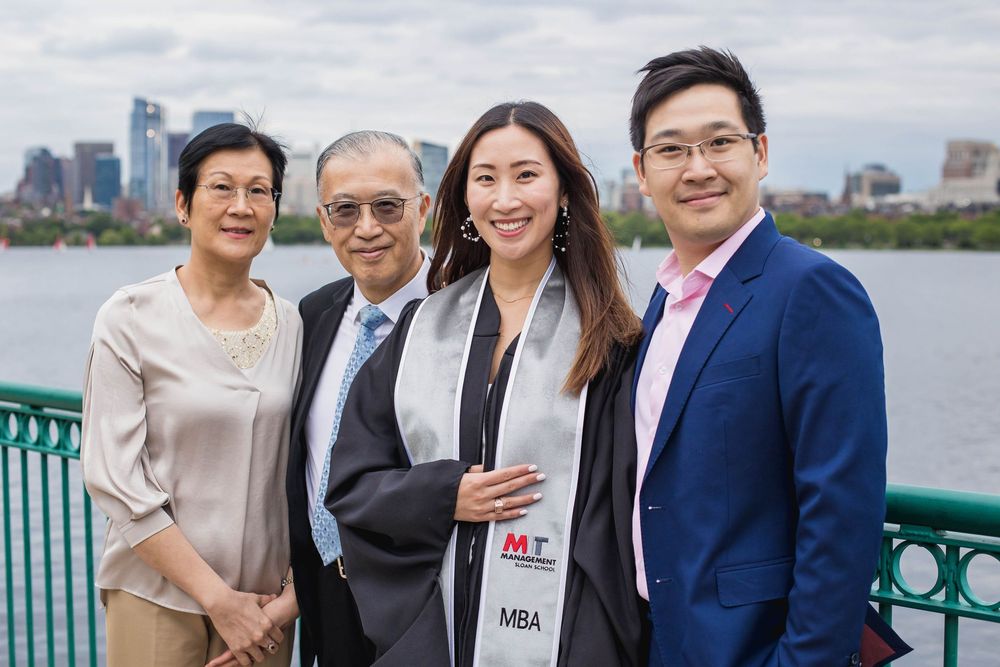 A group of four people smiling outdoors with a city skyline and waterfront in the background.