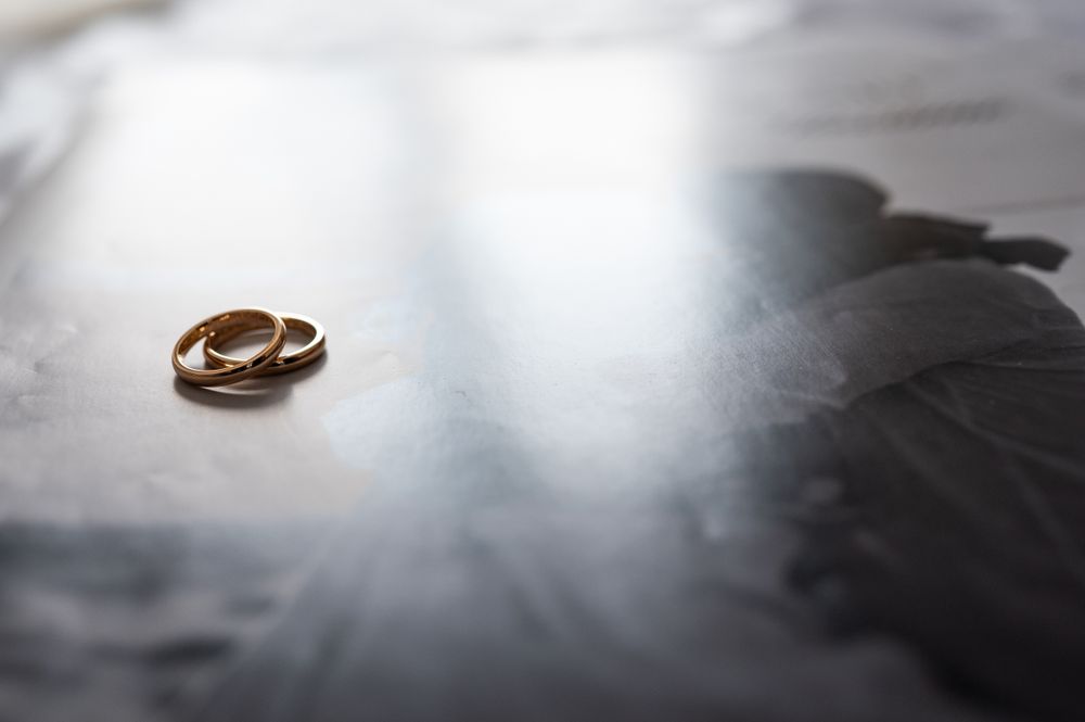 Two wedding rings rest on a soft gray surface in dramatic lighting.