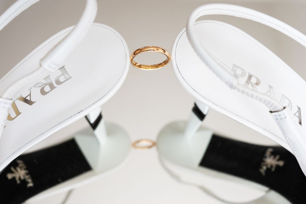Gold wedding ring placed between elegant white bridal shoes.