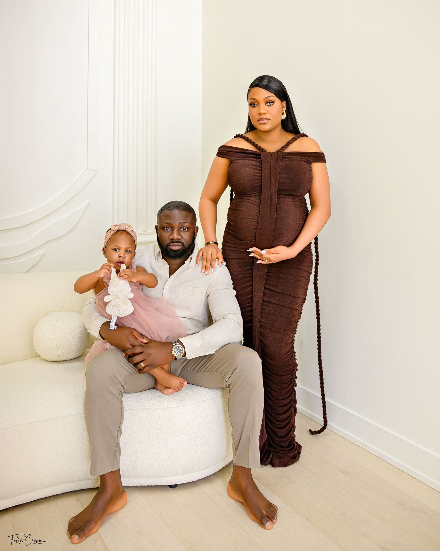 A family poses together in a studio setting with white decor, featuring an elegant brown ruched dress and casual attire.