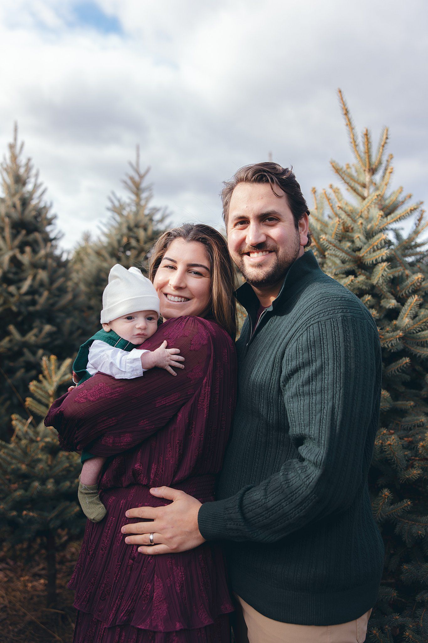Family portrait with baby at Christmas tree farm on cloudy winter afternoon.