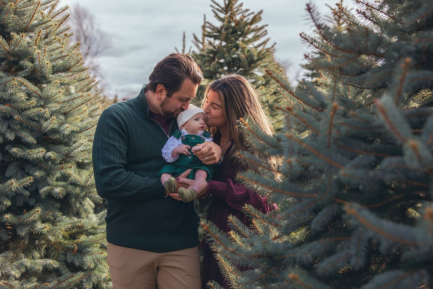 Family shares intimate moment together while surrounded by Christmas trees.