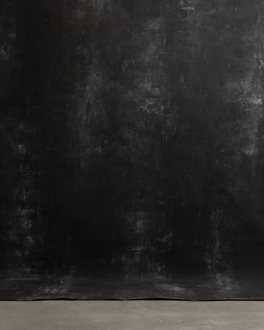 Dramatic black textured backdrop with light concrete floor creating contrast.