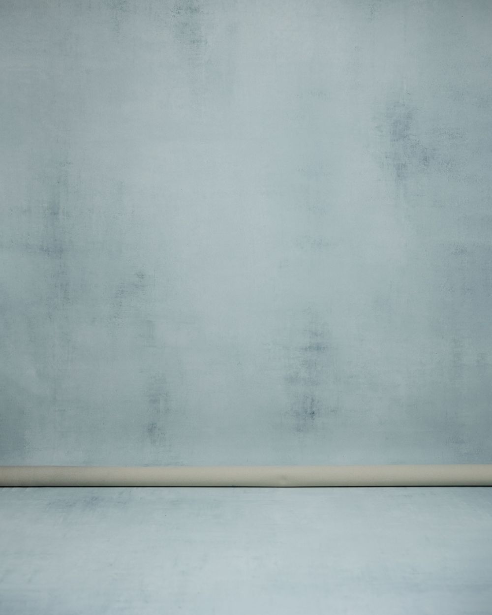 Empty photography studio backdrop with light gray textured wall and wooden baseboard.