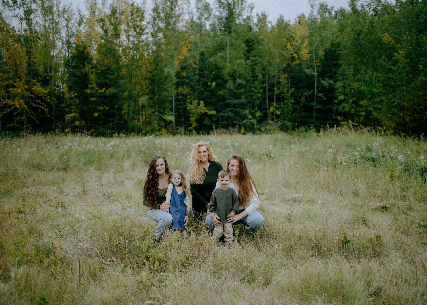 Group sitting together in a grassy field with forest backdrop on an autumn day.