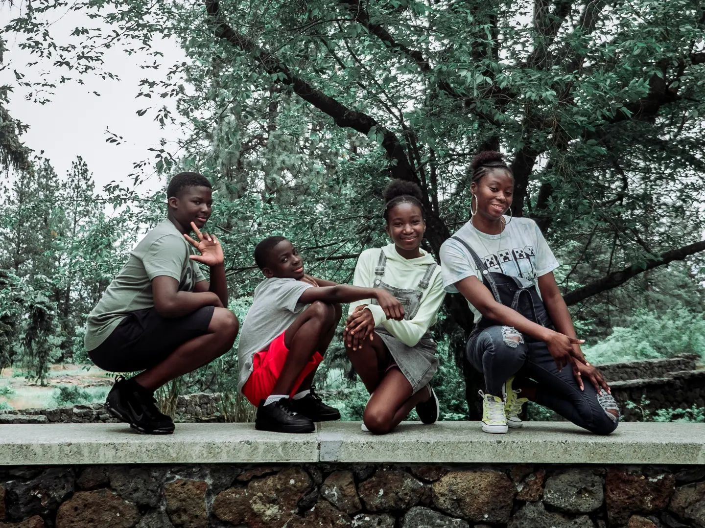 Friends sitting casually on a stone wall surrounded by lush green trees. Family Photography