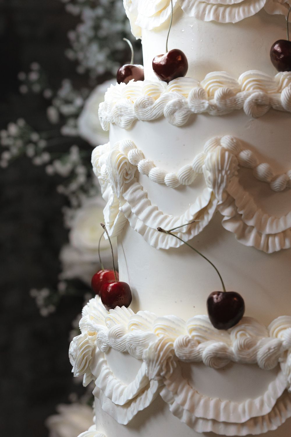 Elegant white wedding cake decorated with ruffled details and fresh cherries.