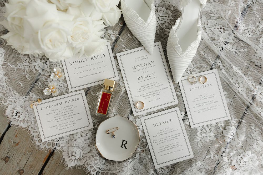 Elegant wedding invitation suite with lace details and rings on wooden surface.