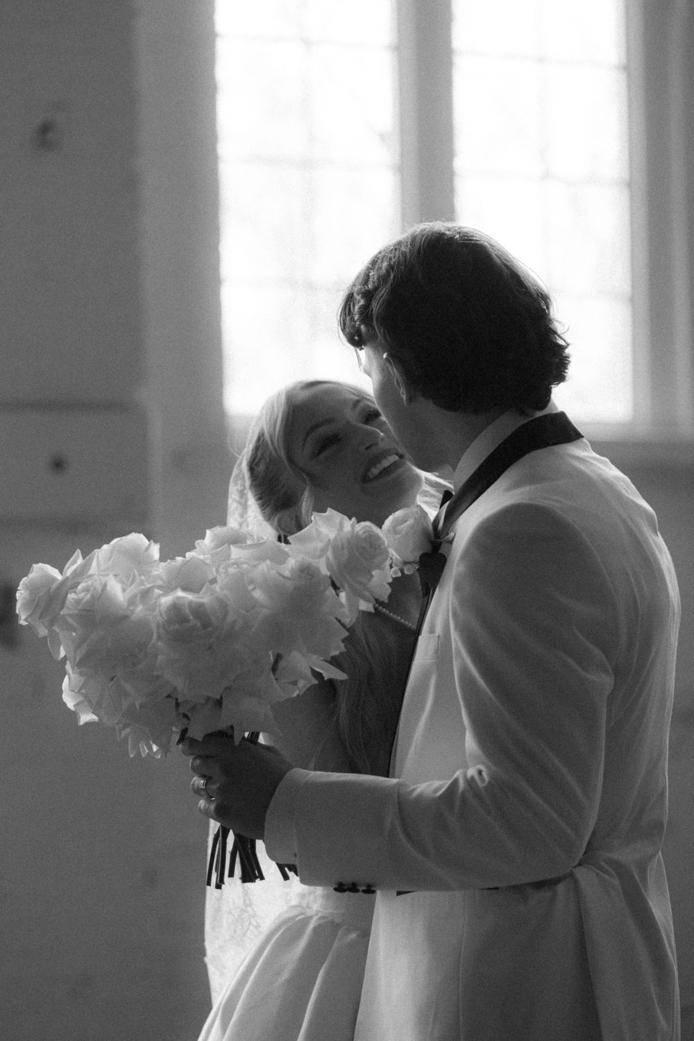 Black and white photo of a romantic wedding moment with white peonies bouquet in natural window light.