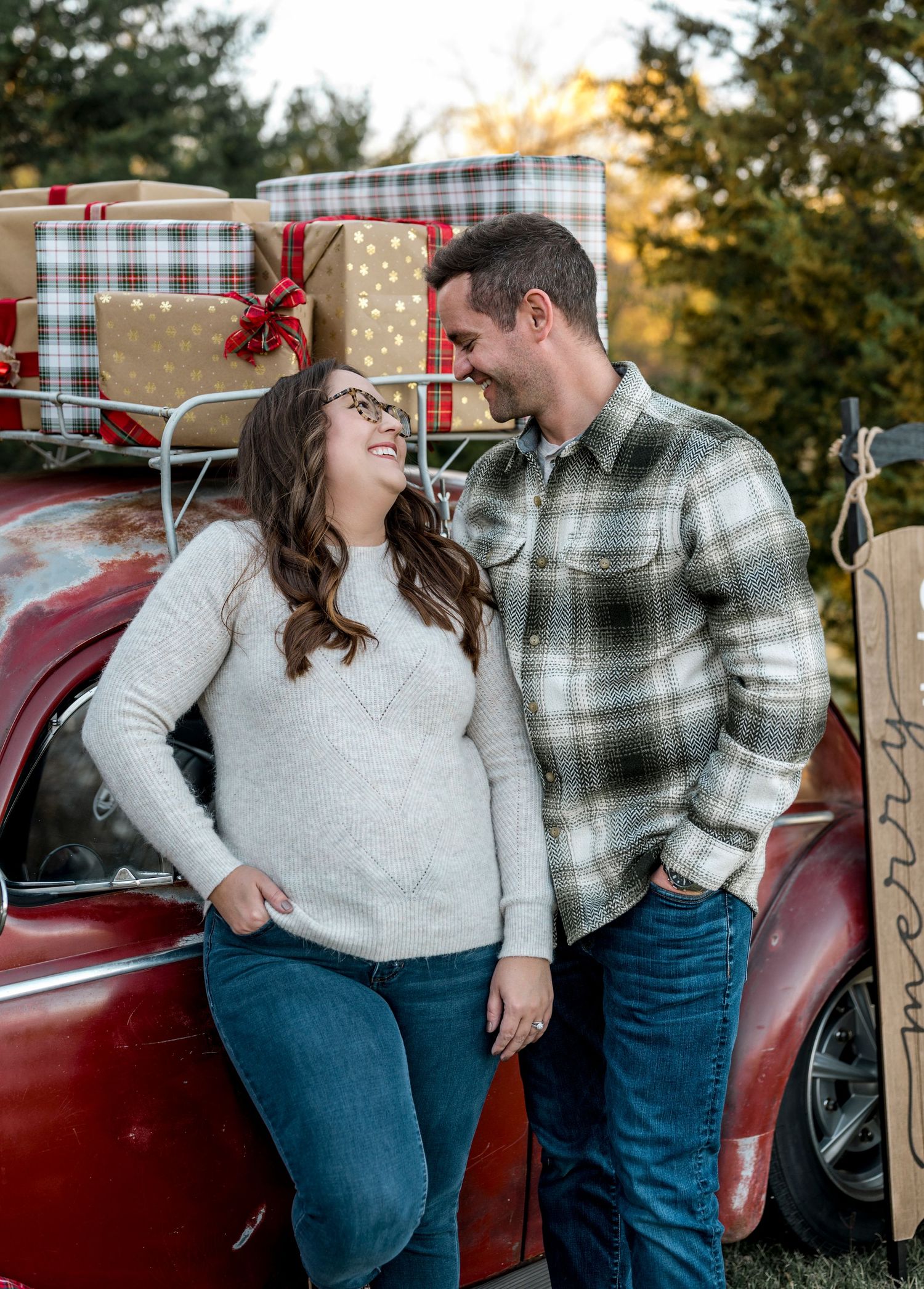 A couple shares a joyful moment together by a red truck filled with wrapped Christmas presents outdoors.
