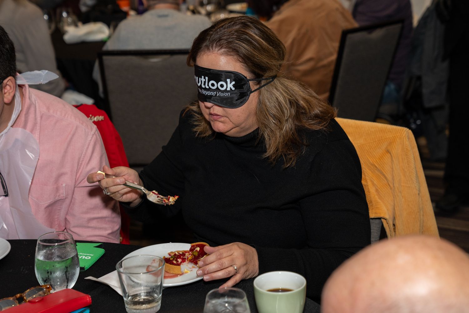 Person eating at a social event while wearing a blindfold.