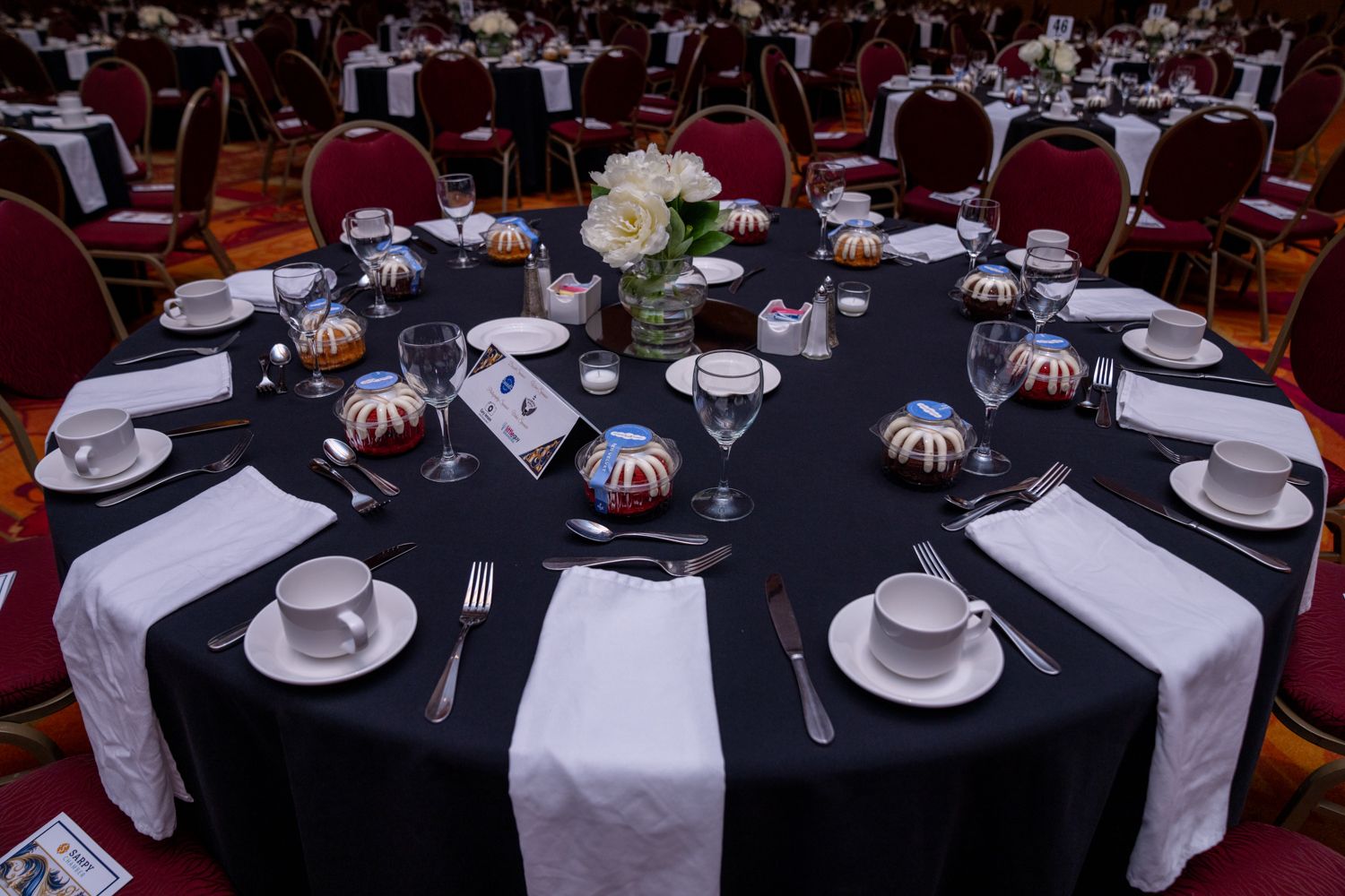 Formal banquet table setting with black tablecloth, white napkins and floral centerpiece in an elegant event space.