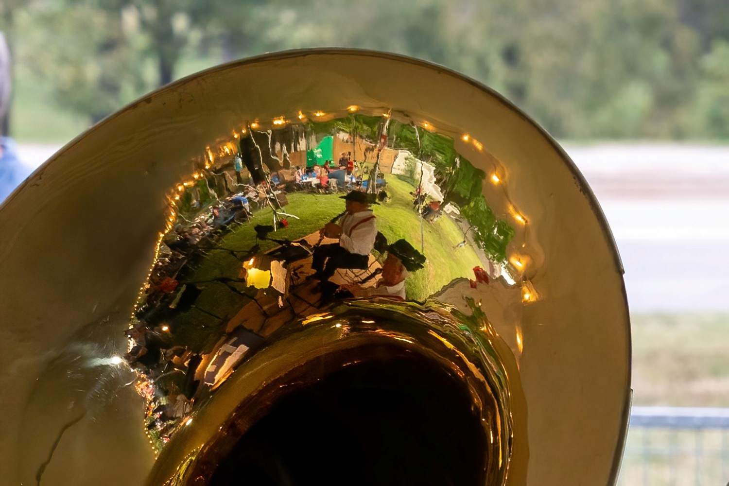 Reflection of an outdoor event scene captured in the bell of a brass instrument.