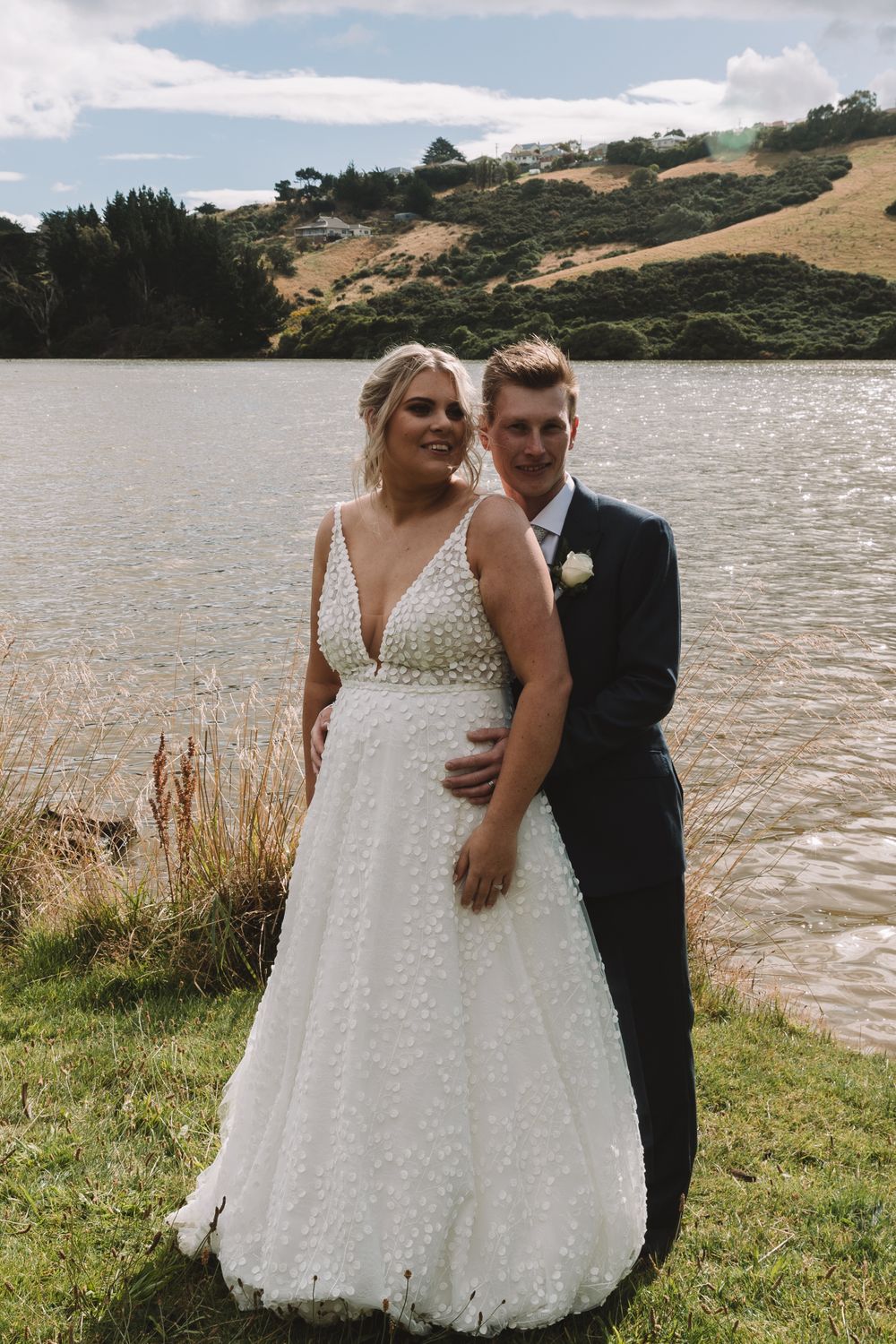 Wedding moment captured by a serene lake with rolling hills in the background.
