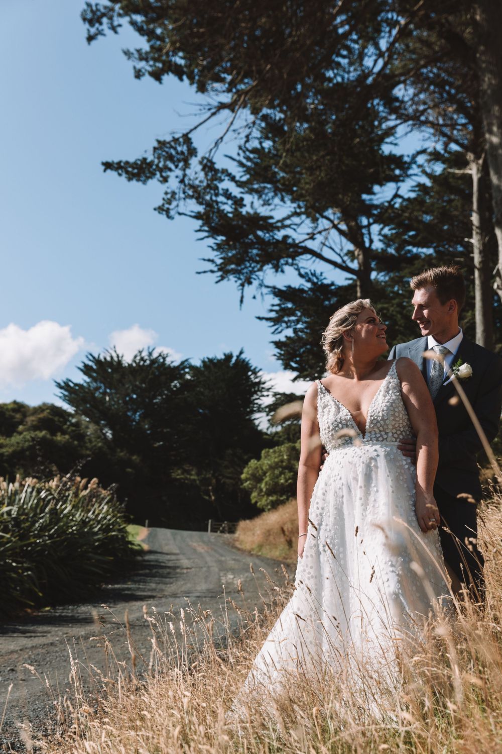 Elegant couple posing on a winding road with cypress trees and golden grass.